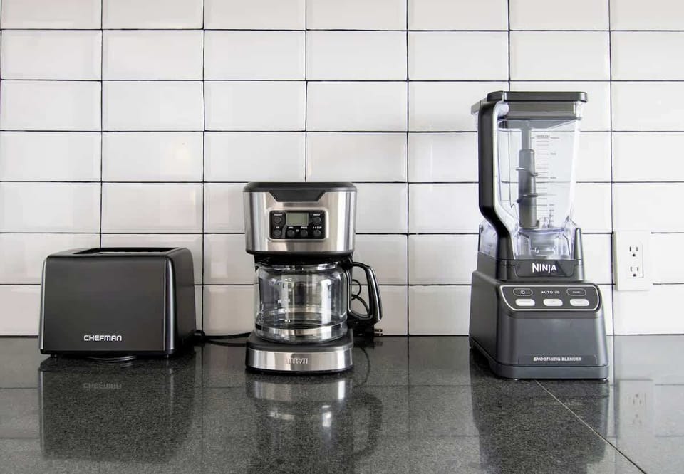 A curated coffee and breakfast station featuring high-end appliances and a sleek tiled backdrop. Every detail—from the stainless finishes to the minimalist layout—reflects both style and thoughtful comfort.