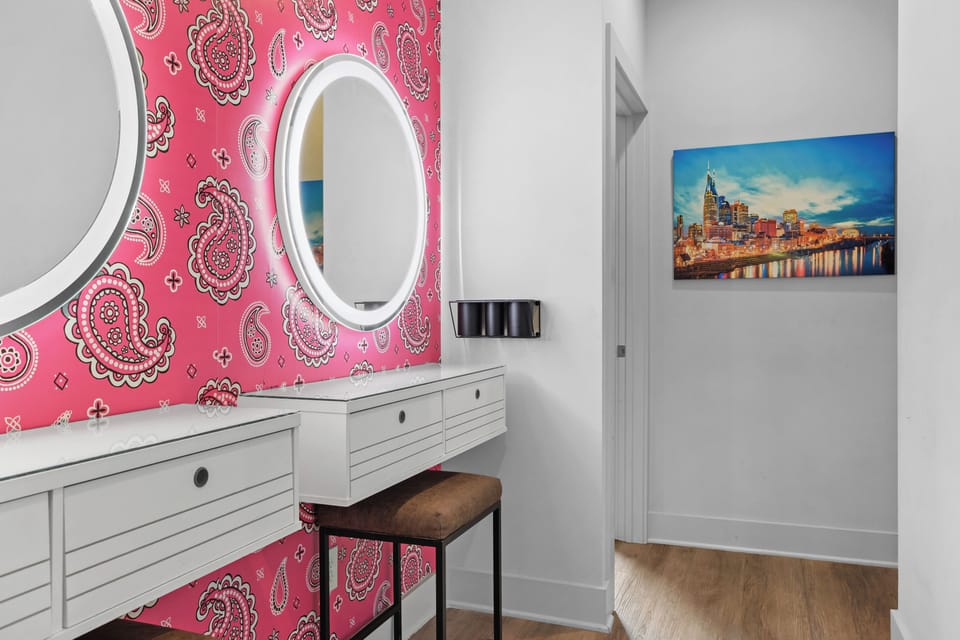 Glamorous makeup station with bold wallpaper, lighting, and a stool.