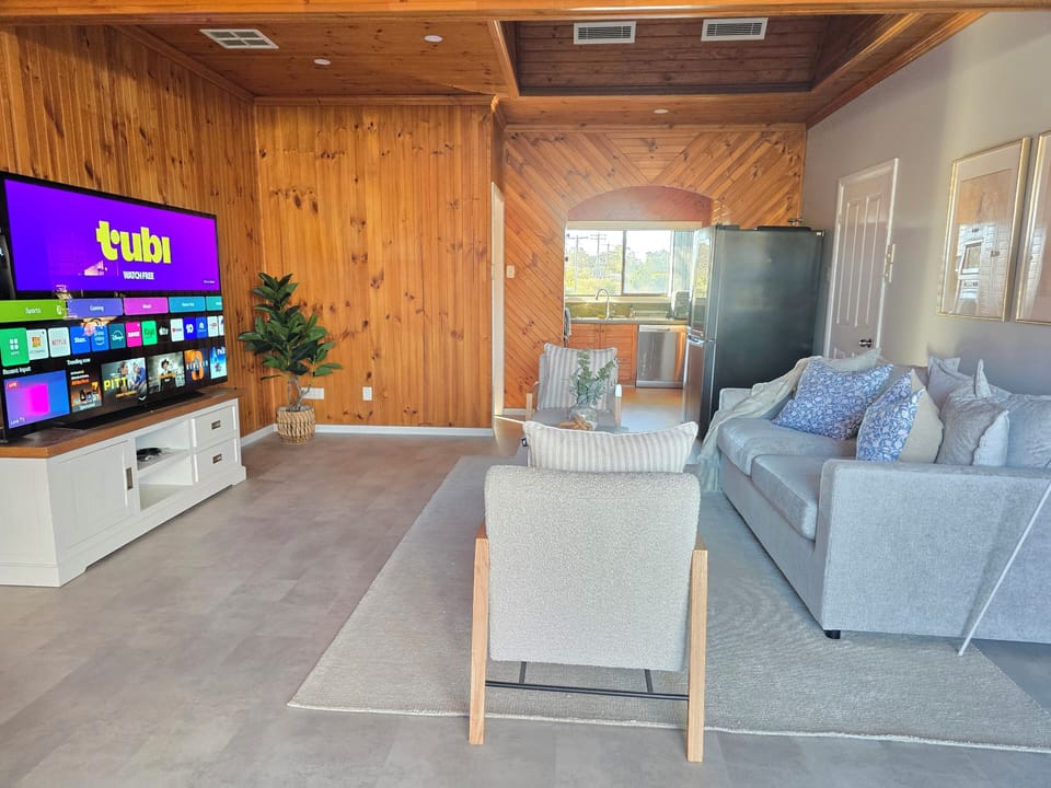  Spacious shared living room with large TV, comfy seating, and garden views.