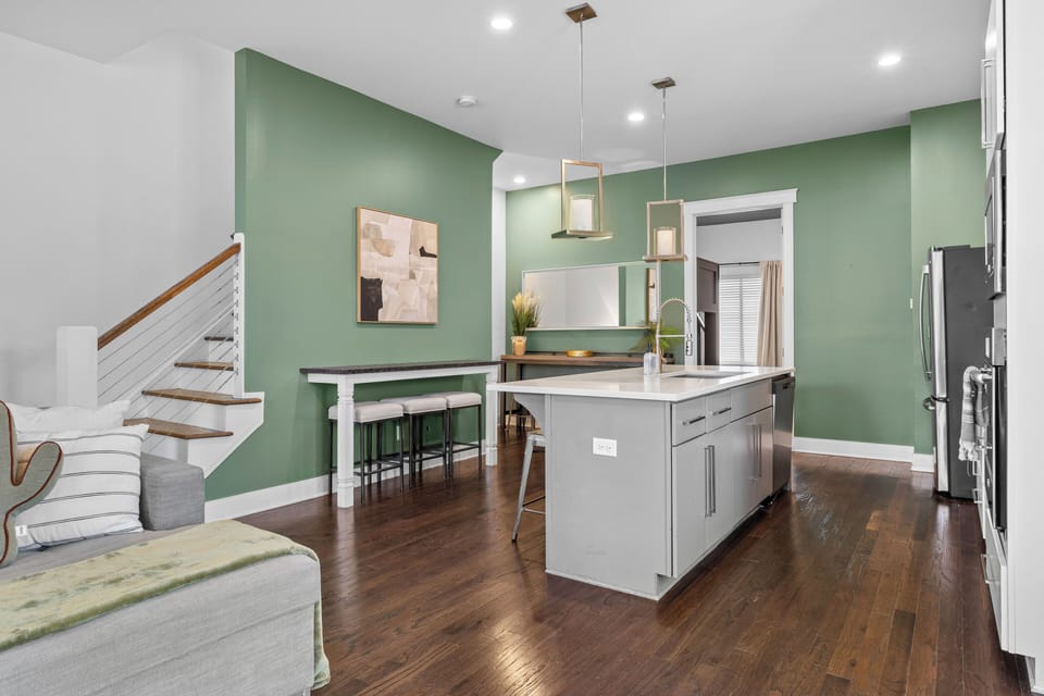 Modern green kitchen with quartz island, bar seating & hardwood floors

