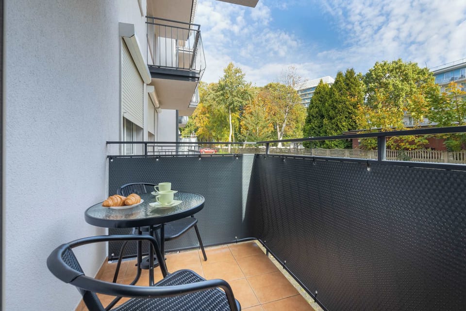 A small balcony with a table and two chairs overlooking trees. The outdoor space feels private and peaceful.