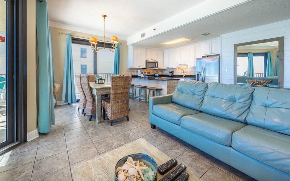 Bright living space featuring a turquoise sofa, dining area with woven chairs, and a modern breakfast bar for entertaining