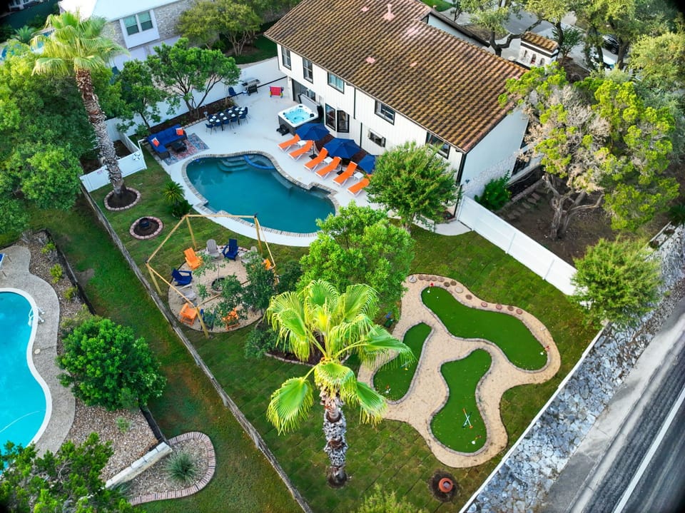 Soak in the resort vibes! An aerial view of The Comfy Coyote’s backyard oasis with private pool, mini golf, hot tub, firepit, outdoor dining, loungers, and plenty of space to relax and play together.
