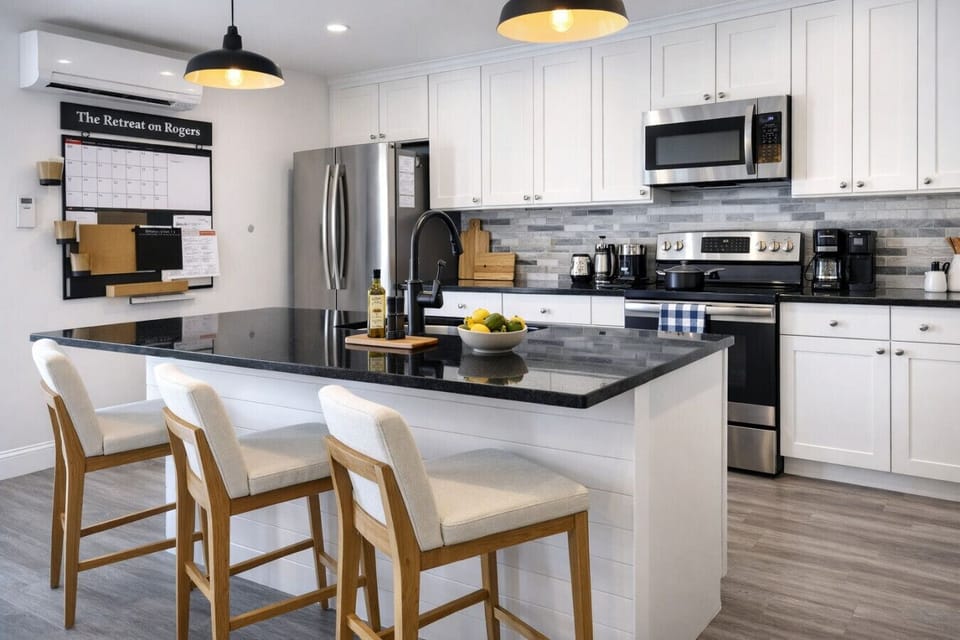 Cook and gather in this bright modern kitchen featuring a large central island with black countertops and comfortable bar seating for three. The fully equipped space includes stainless steel appliances, ample white cabinet storage, and everything you need