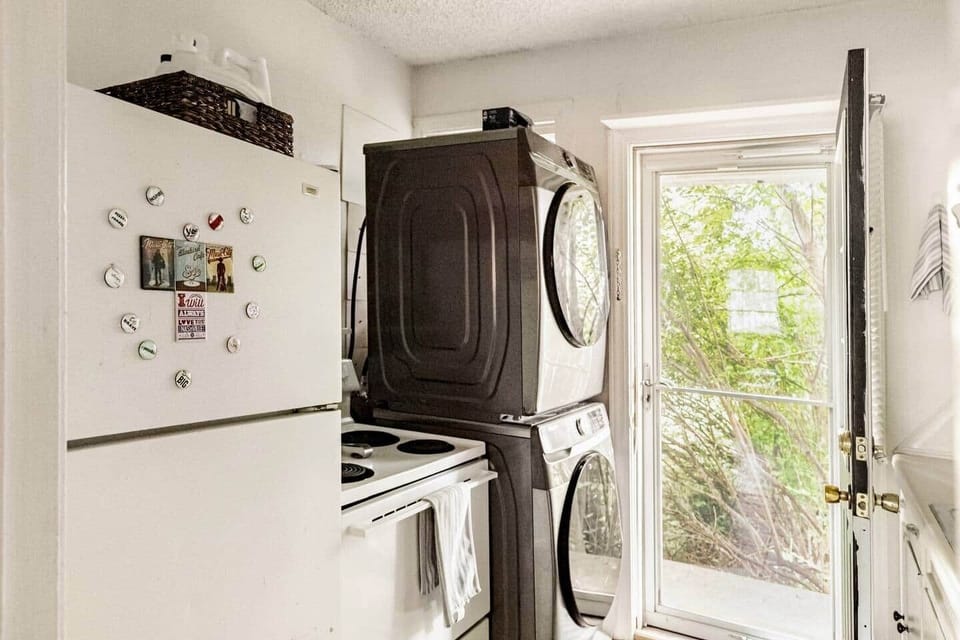 A convenient laundry area with a stacked washer and dryer, a refrigerator with fun magnets, and complimentary laundry detergent & softener. The windowed door brings in natural light, making this space bright and functional for your stay.