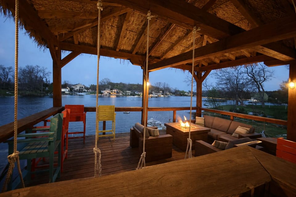 Covered lakefront tiki deck with seating, lights, and stunning sunrise views