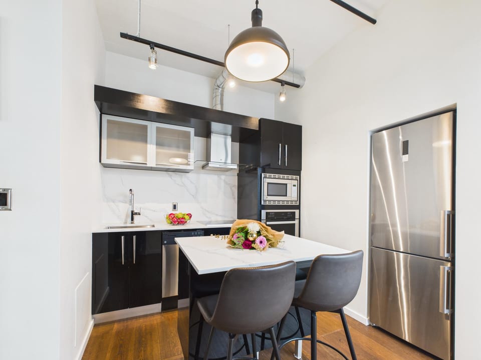 A chef's dream! This modern kitchen boasts sleek dark cabinetry, bright white countertops, and a central island breakfast bar.