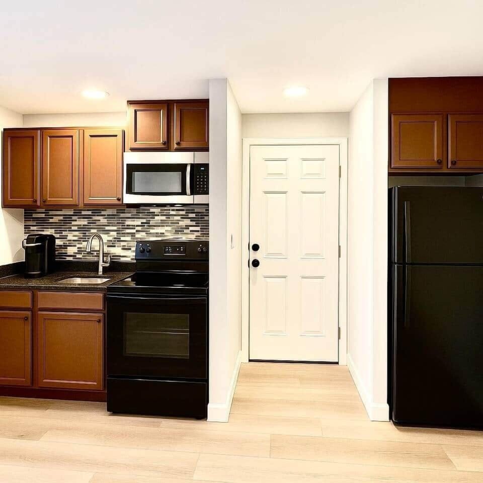 Modern kitchen with dark wood cabinets, black appliances, a sleek tile backsplash, and a Keurig coffee maker. Fully equipped with dishes, cookware, and utensils — clean, stylish, and ready for your stay.