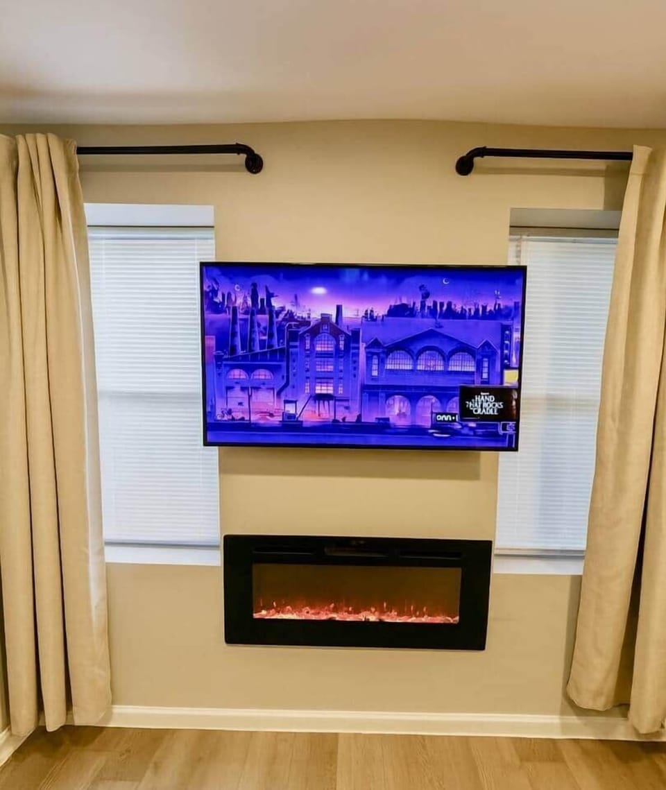 Cozy modern living room with a futon sofa, flatscreen TV, and electric fireplace for a warm, relaxing stay.