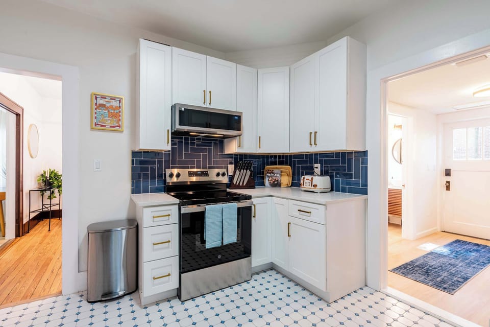 Modern, well-equipped kitchen featuring crisp white cabinetry, vibrant blue backsplash, and sleek stainless steel appliances.