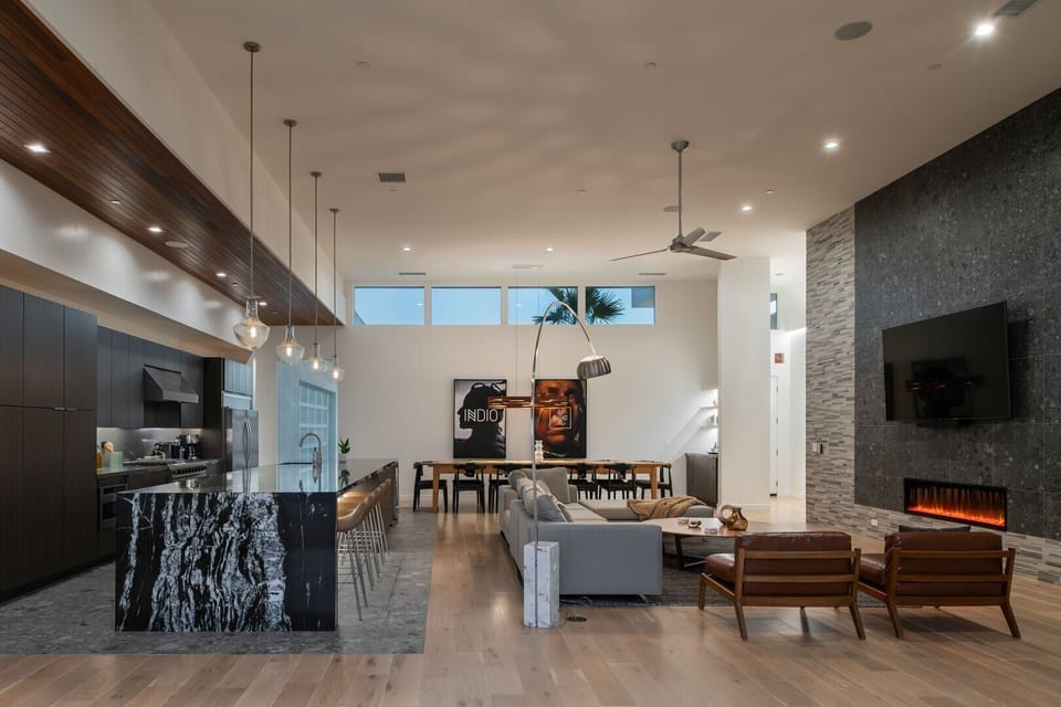 The expansive open-concept great room, featuring soaring ceilings, a modern fireplace, and seamless flow between the kitchen and living areas.