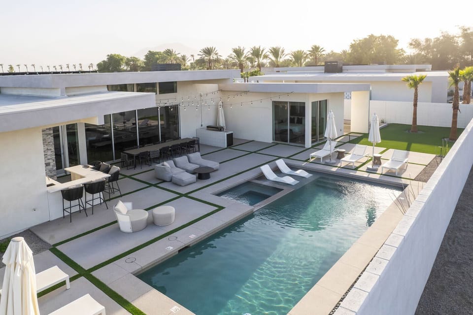 An elevated view of the resort-style backyard in the morning sun, showcasing the pool, spa, outdoor bar, and various lounge areas.