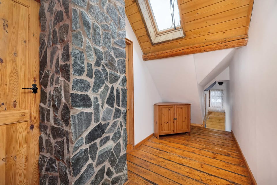 A view down a narrow wooden staircase with stone walls. The design emphasizes the mountain-cabin aesthetic.