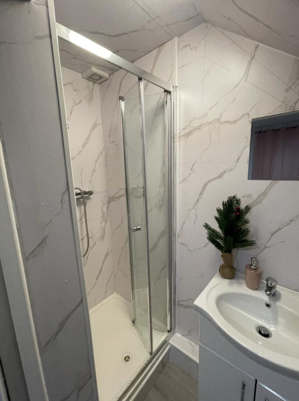 Enclosed shower with white marble tiling and sink