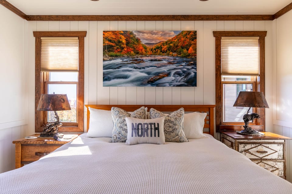 Wake up to mountain charm in this king bedroom, where rustic lamps and a bold North Carolina river print set a cozy Blue Ridge mood.