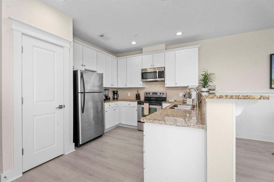 Modern kitchen featuring stainless steel refrigerator, microwave, range, granite counters, and functional open-concept layout.