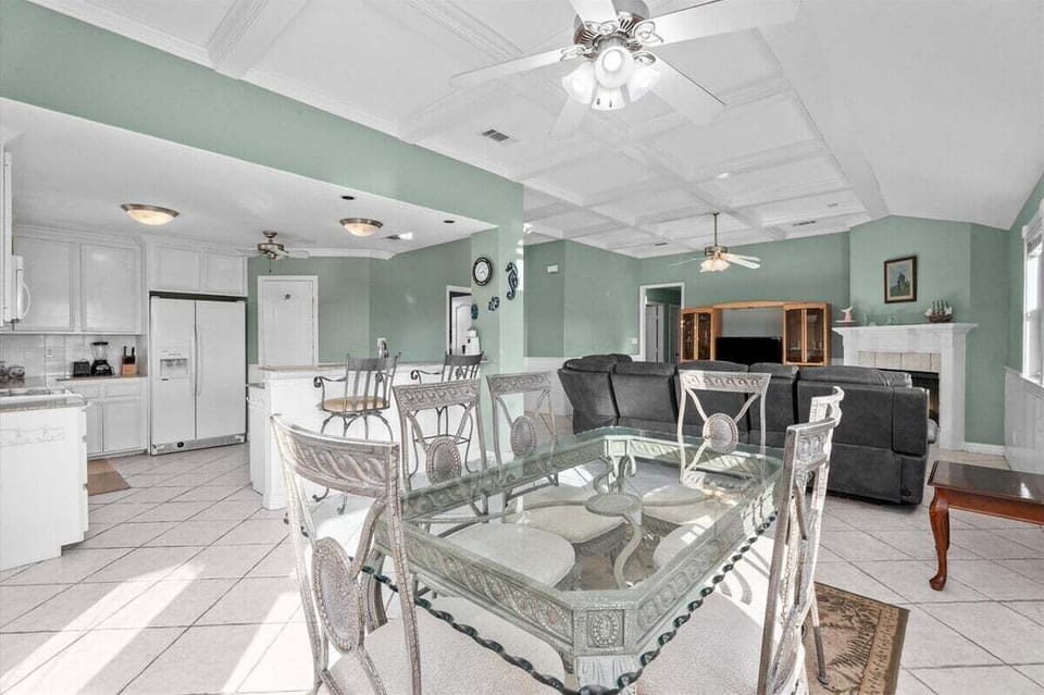 Bright open floor plan with dining table, kitchen, living room, ceiling fans, and tile flooring for easy group gathering.