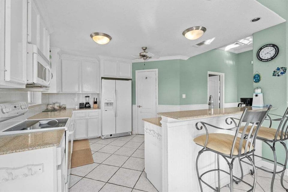 Kitchen view with white cabinetry, microwave, refrigerator, bar seating, and open access to the main living area.
