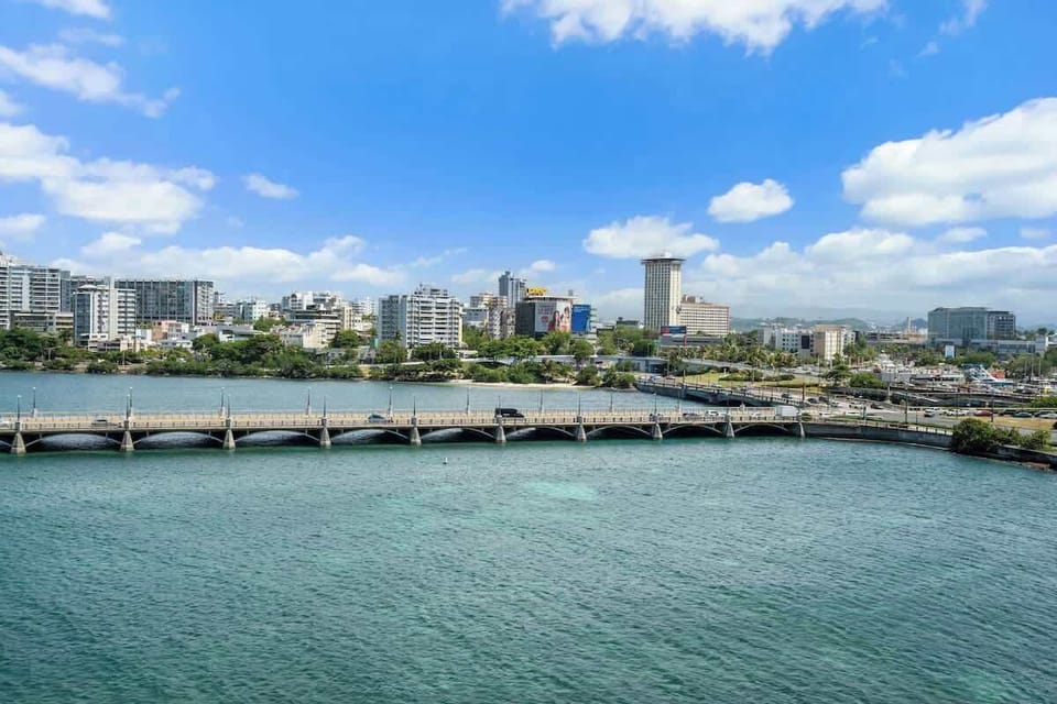 Enjoy the unique vantage point where city vibrancy meets coastal tranquility, all under a beautiful clear sky with fluffy white clouds.