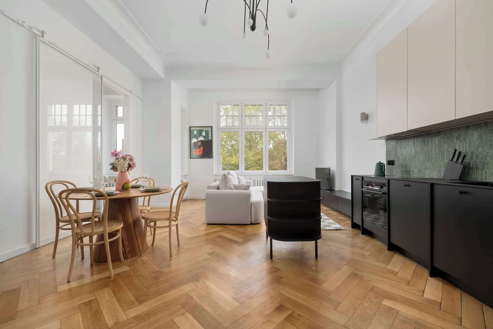 A wide-angle view of the kitchen and dining area, showcasing modern black cabinetry and vintage wooden doors. The combination feels both elegant and rustic.