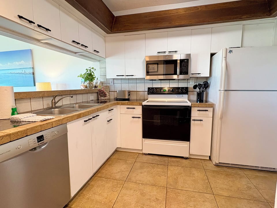 Kitchen with white cabinets, stainless steel microwave, range, and refrigerator