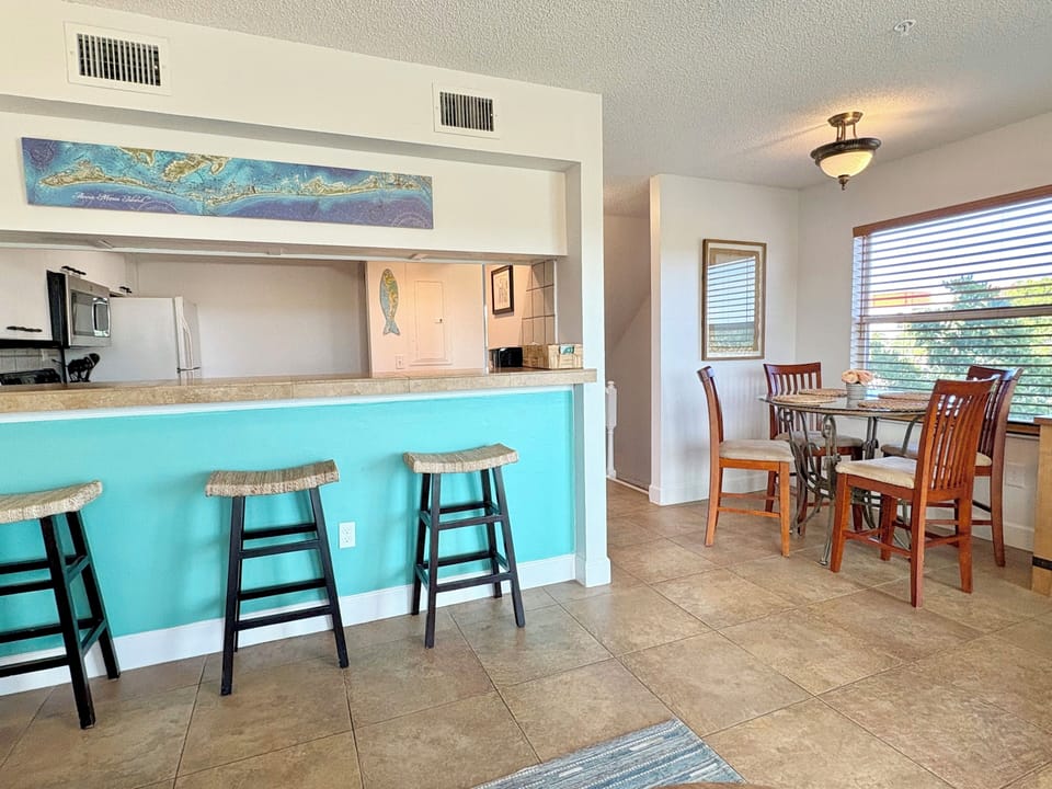 Kitchen and bar area with bar stools, teal accent tile, overhead cabinets, and adjacent dining space
