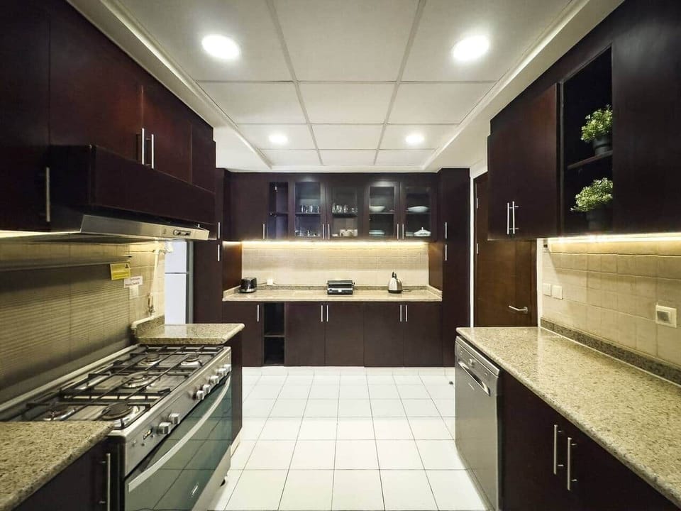 Spacious kitchen with sleek dark wood cabinets, granite countertops, and under-cabinet lighting. Fully equipped with a large gas stove, modern appliances, and all essentials for a comfortable cooking experience.