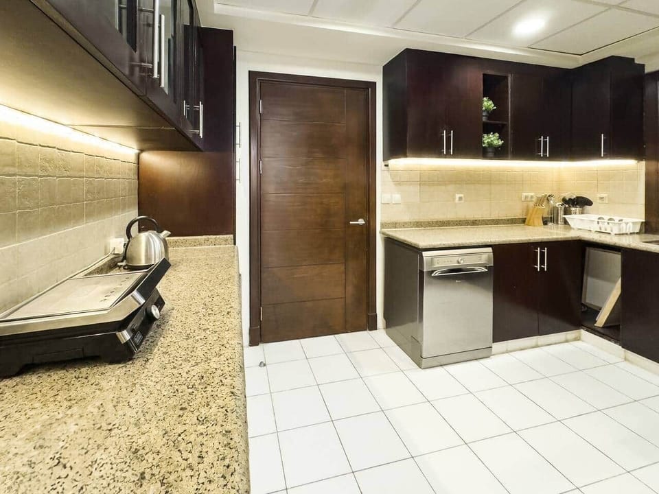 Modern kitchen with dark wood cabinets, granite countertops, and warm under-cabinet lighting. Fully equipped with stainless steel appliances, a kettle, and cooking essentials—perfect for a comfortable and convenient stay.