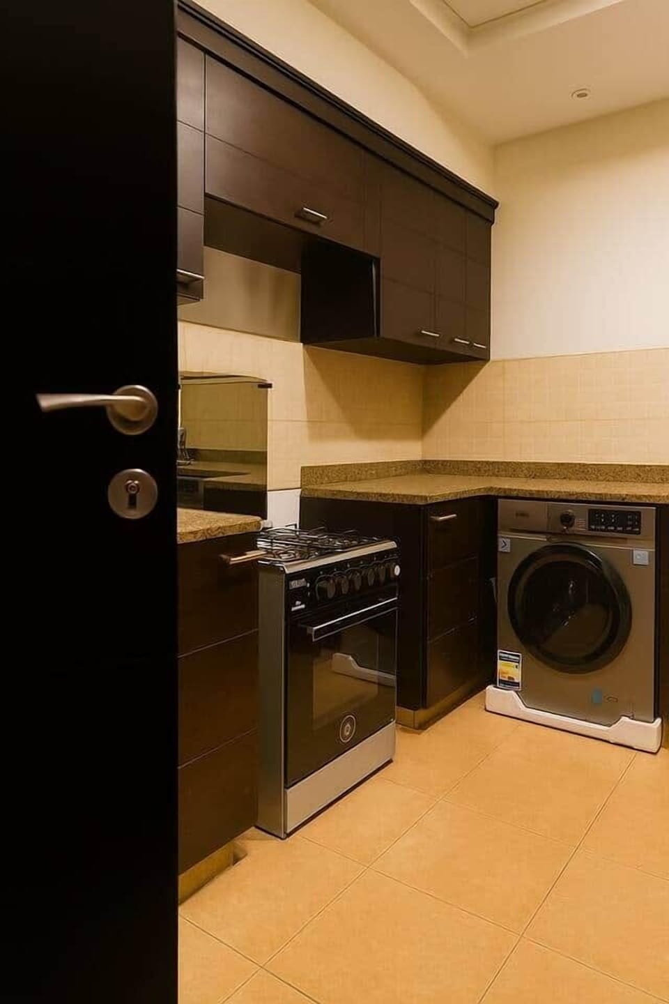 A stylish and well-equipped kitchenette with granite countertops, dark wood cabinets, warm lighting, and essential modern appliances.

