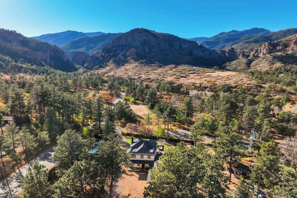 A breathtaking aerial view reveals the home tucked among towering pines with dramatic mountain ridges stretching beyond.