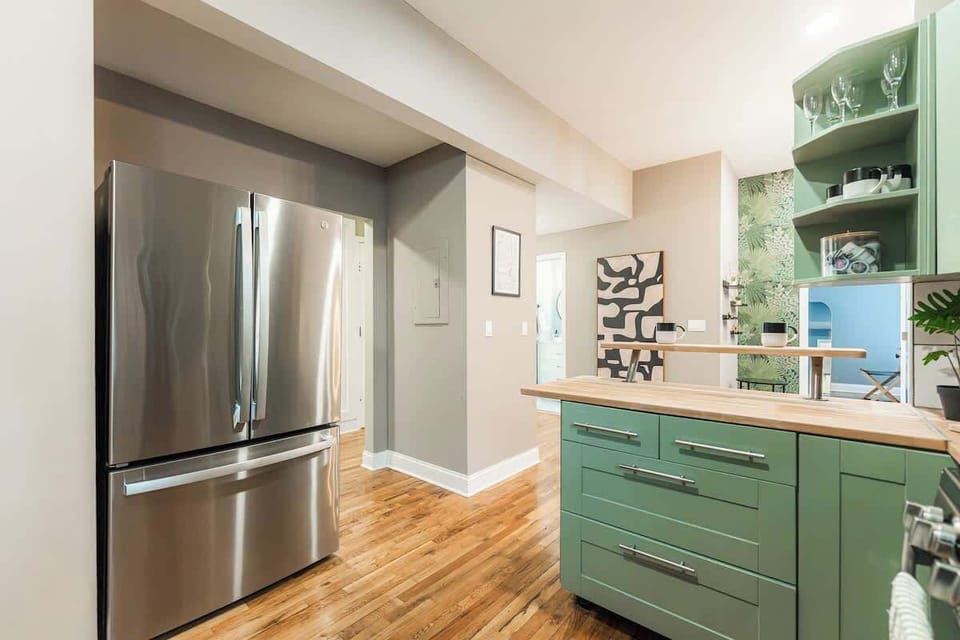 Fully equipped kitchen with stainless steel fridge, sage green cabinetry, and wood countertops. Clean, modern space with ample storage and easy flow—perfect for preparing meals comfortably.
