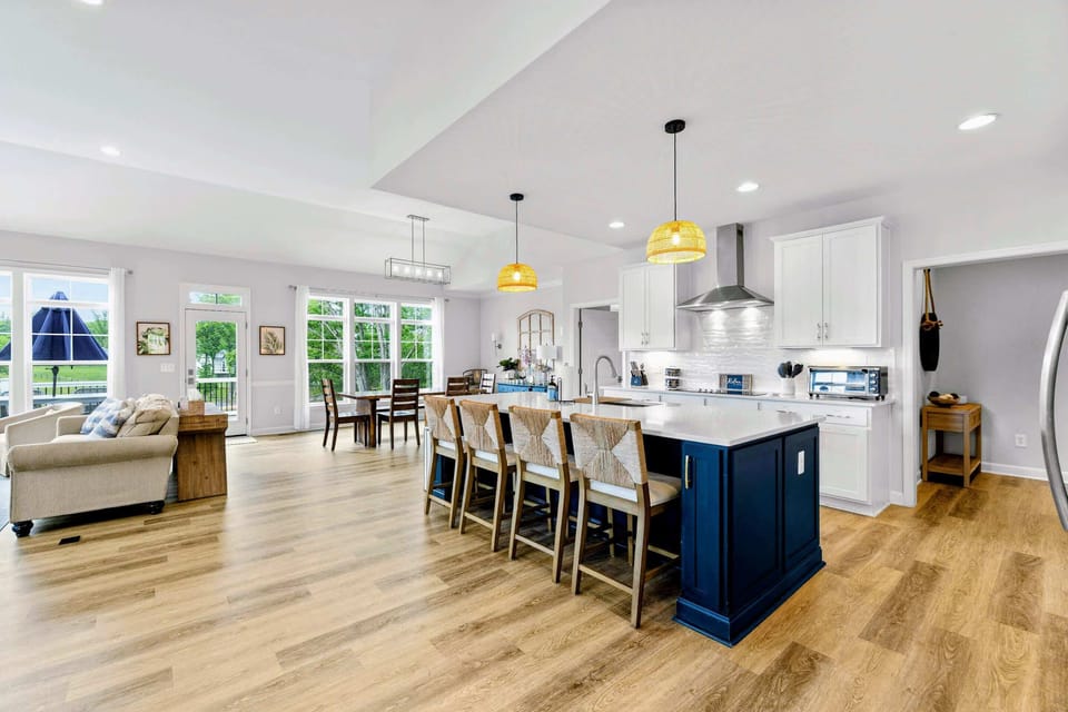 Kitchen - Navy island with woven barstools, rattan pendants, and quartz counters anchors the open living and dining space.