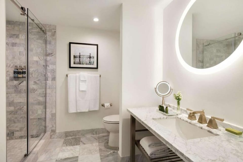 Bathroom with glass shower, marble counter, and round mirror