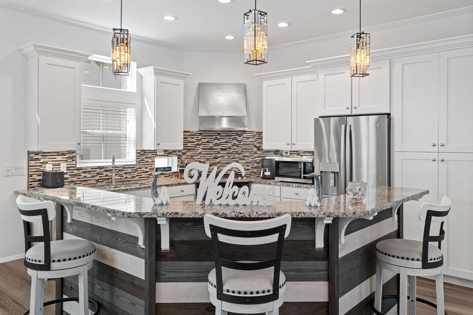 Elegant coastal kitchen with granite countertops, stainless steel appliances, and a shiplap island accented by pendant lighting—inviting guests to gather, cook, and enjoy time together.