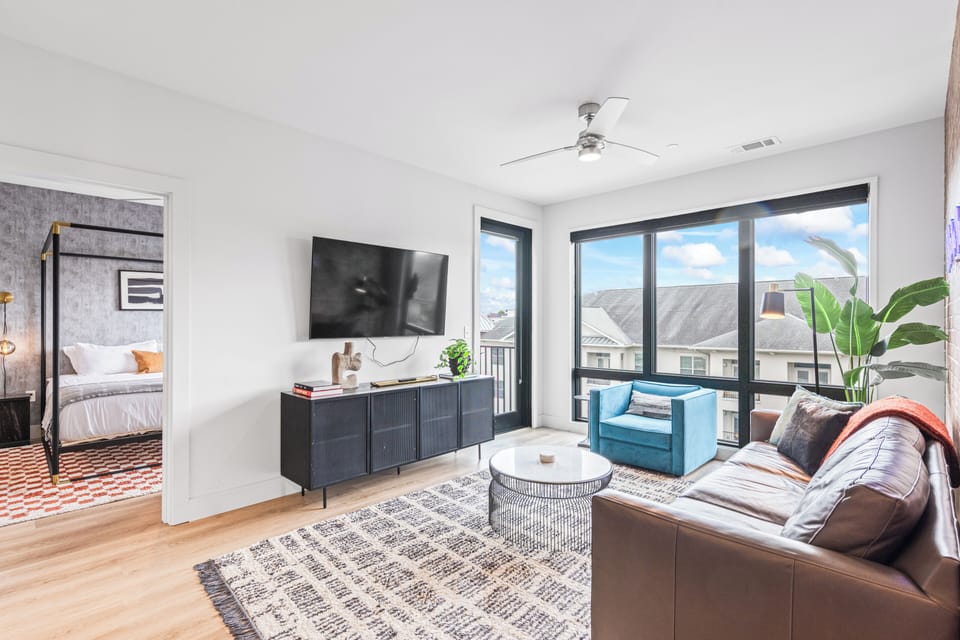Bright living area with TV, sectional sofa, and balcony access.