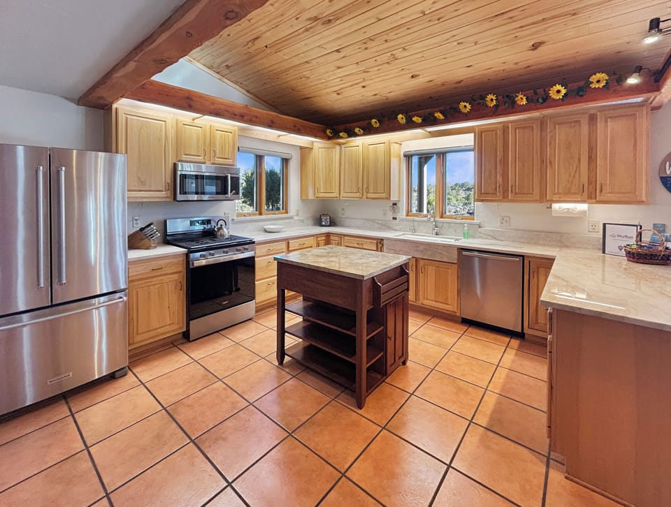 Step into this warm, rustic kitchen where exposed wooden beams and golden sunflower accents create a cozy mountain retreat atmosphere. You'll love cooking with stainless steel appliances while enjoying natural light streaming through the windows.