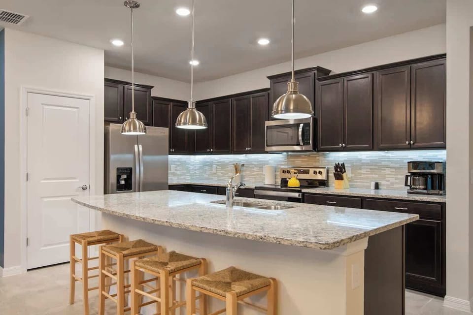 Gather around this bright, modern kitchen designed for shared moments. Cook together on spacious stone counters, enjoy morning coffee at the island, and laugh over family meals with stainless appliances for all.
