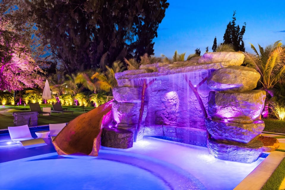 “Unwind in your own private resort—featuring a grotto waterfall, waterslide, and vibrant evening lighting.”

