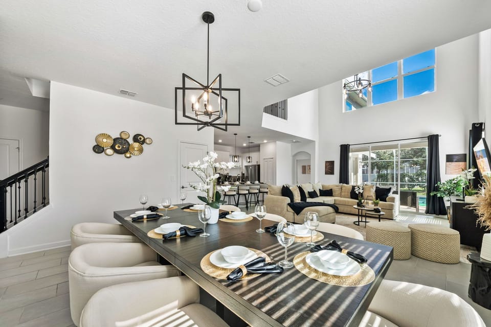 Open-concept elegance: dine at the table for 8 under a geometric chandelier while the airy living room with tall windows and a plush sectional invites you to relax.
