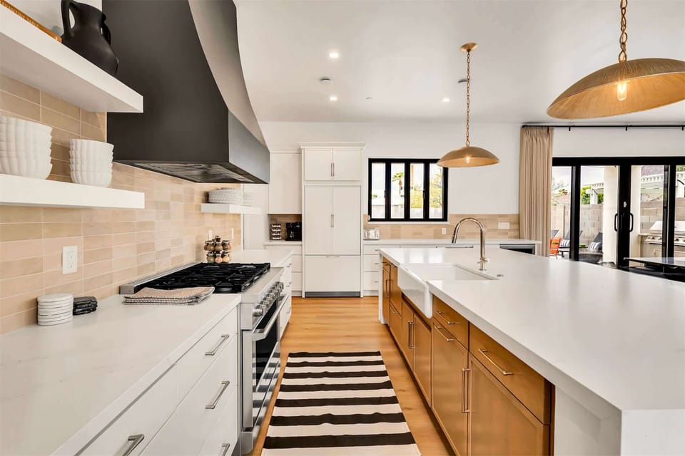 Kitchen with gas stove, exposed shelving, large island. Serving window to back patio