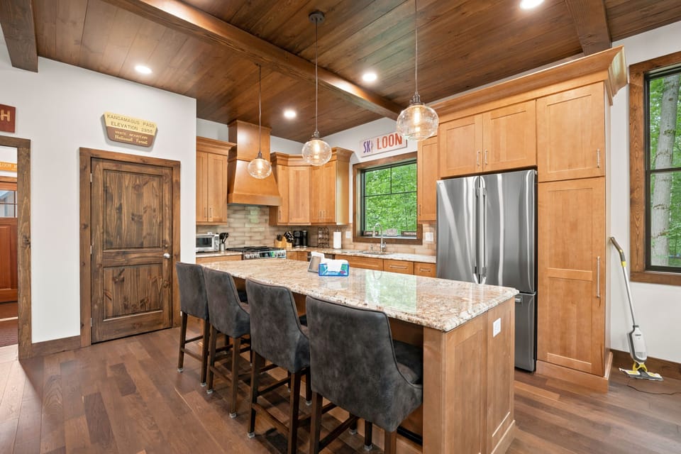 Bright, modern kitchen with stainless steel appliances and a large granite island. Perfect for group cooking, morning coffee, and family-style dining with forest views.