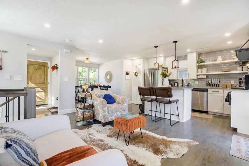 Open living room and kitchen layout with a large island, bar stools, and comfortable seating—ideal for cooking, chatting, and relaxing together in a bright space filled with natural light.