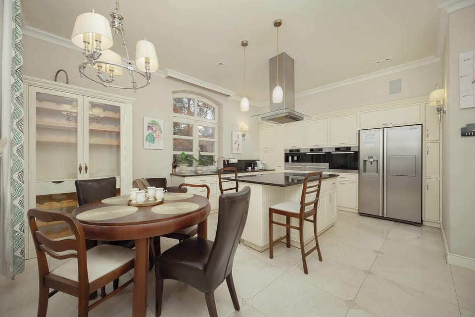 A bright and spacious kitchen with a wooden dining table and pendant lighting. White cabinetry and appliances maintain a clean aesthetic.