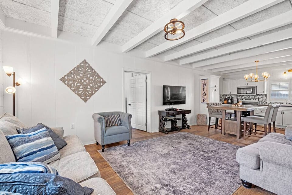 The living room features a deep, plush sofa, matching loveseat, and a cozy upholstered reading chair. An open floor plan and big-screen Smart TV create a comfortable, inviting space to relax.