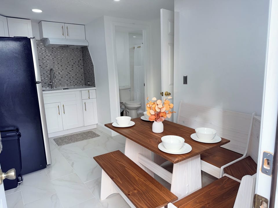 Your bright, modern kitchen awaits with sleek white cabinets and stylish tile backsplash. Gather around the warm wooden dining table for morning coffee or evening meals, with everything you need just steps away.