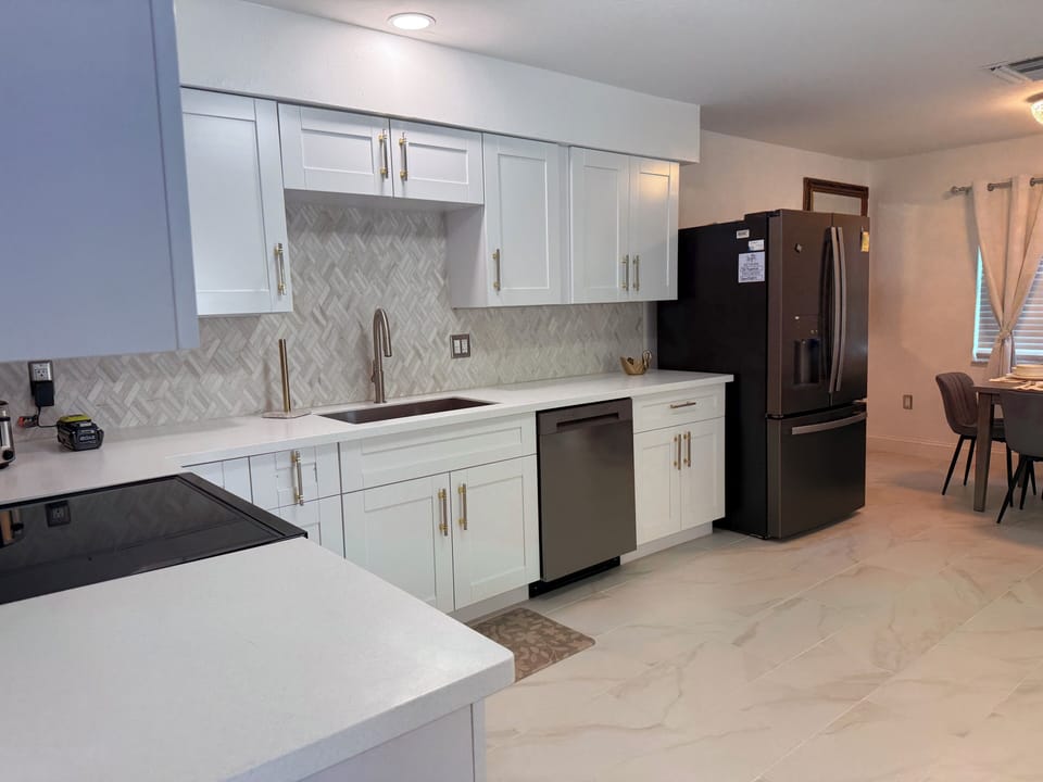 Equipped modern kitchen with gleaming white cabinets, quartz countertops, stainless steel appliances.