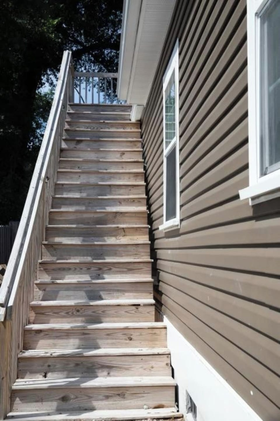 Outdoor wooden staircase leading up to a brown-sided house.