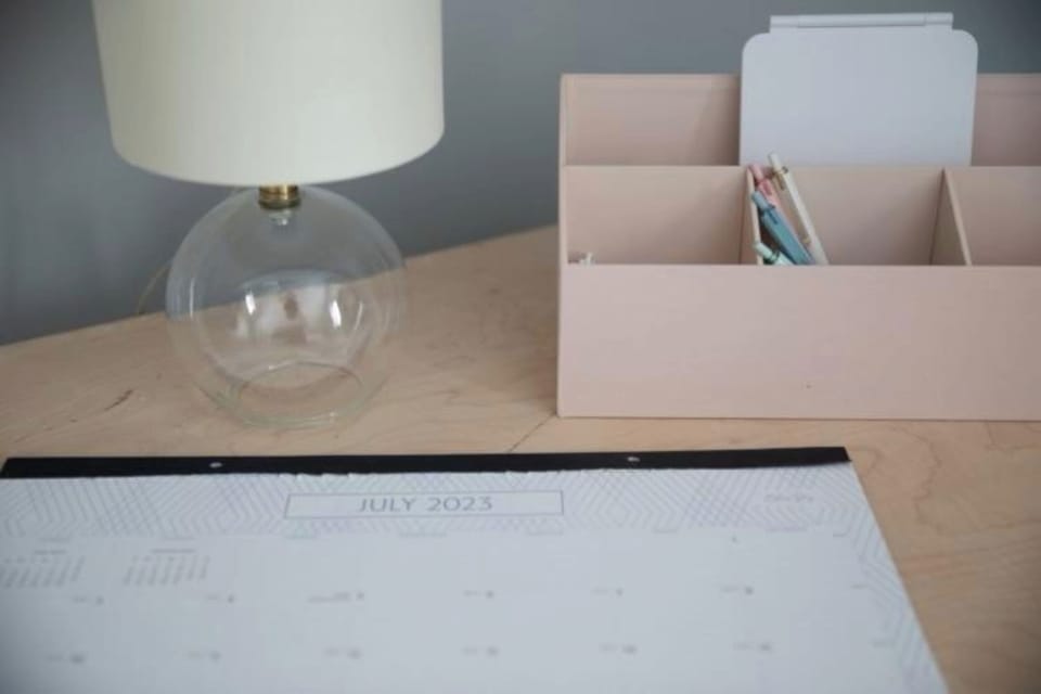 Desk organizer, lamp, and calendar for July 2023 on a wooden desk.