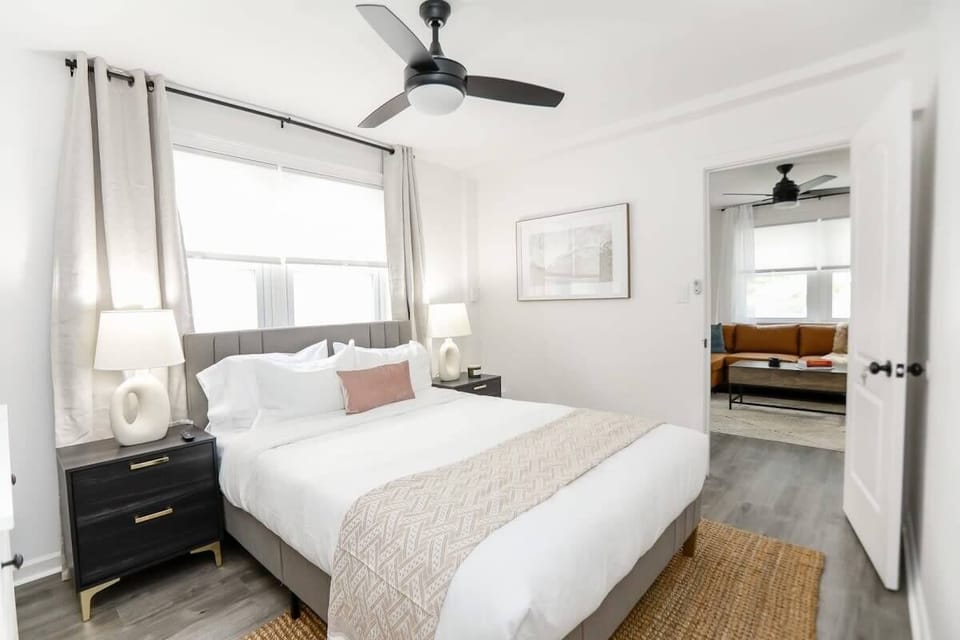Bedroom with end tables, lamps, ceiling fan, and a large window. 