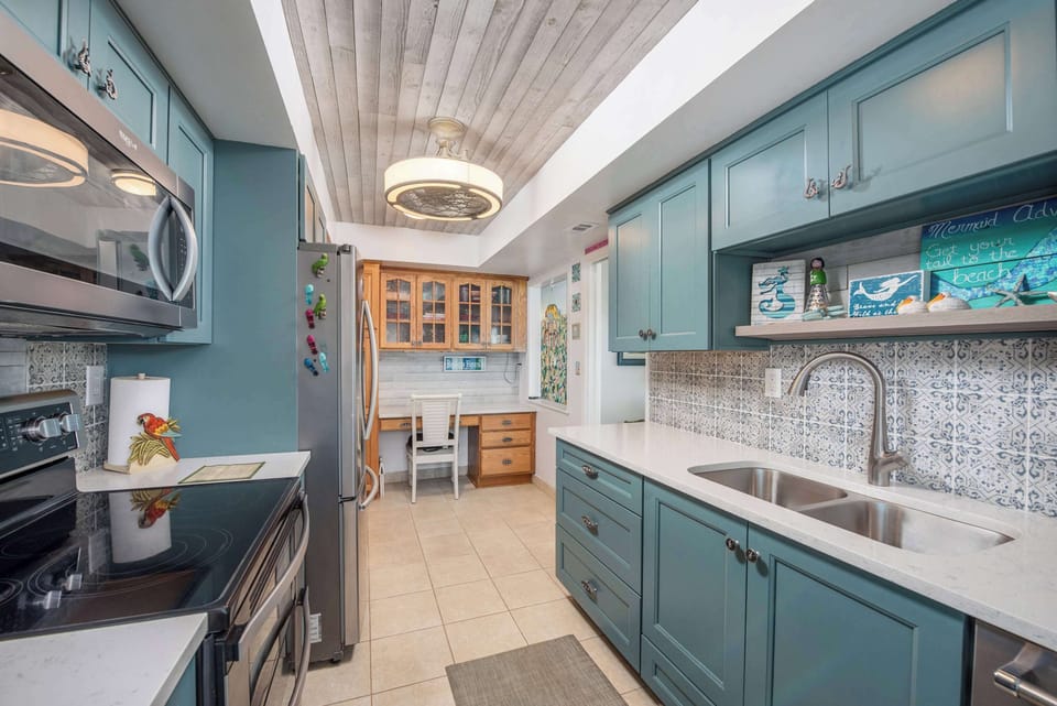 Coastal kitchen with teal cabinetry, patterned tile backsplash, and a built-in desk area.